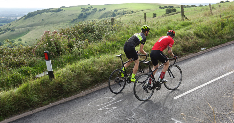 Two cyclists riding together on their Orro Bikes up a steep hill on a hot summers day