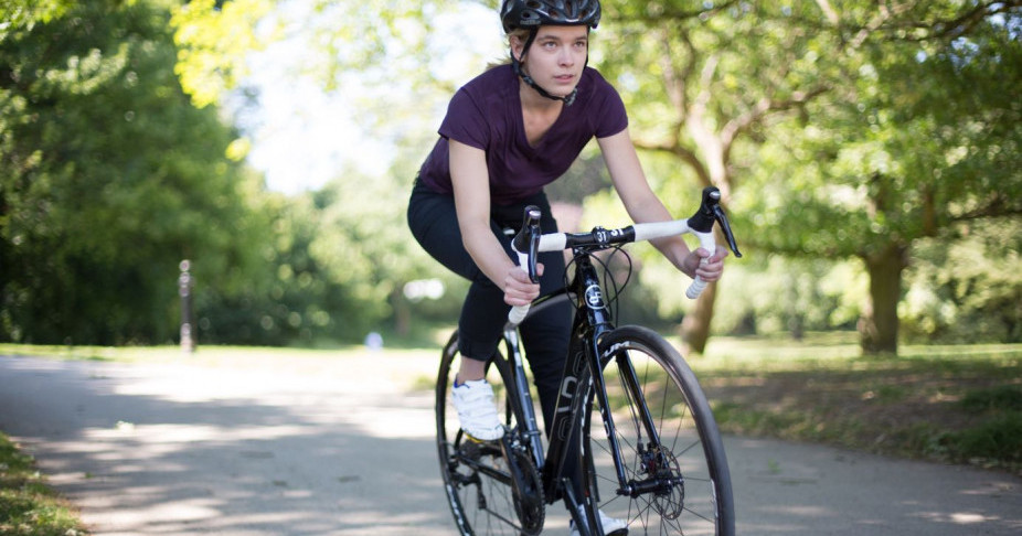 Female cyclist making her way through a park on a summers day on her Orro Bike wearing Fox Wilson's purple Cromwell T-Shirt