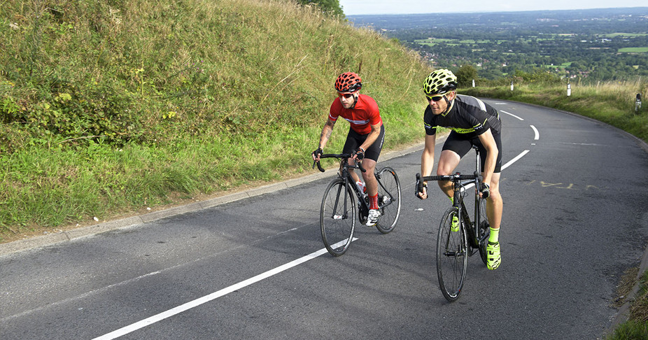 Two riders wearing full biking gear riding up a hill on a summers day