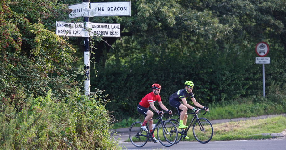 Two cyclists riding side-by-side going up a hill in Ditchling
