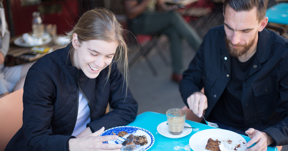 Two casual cyclists wearing Fox Wilson clothing enjoying some cake at a cafe