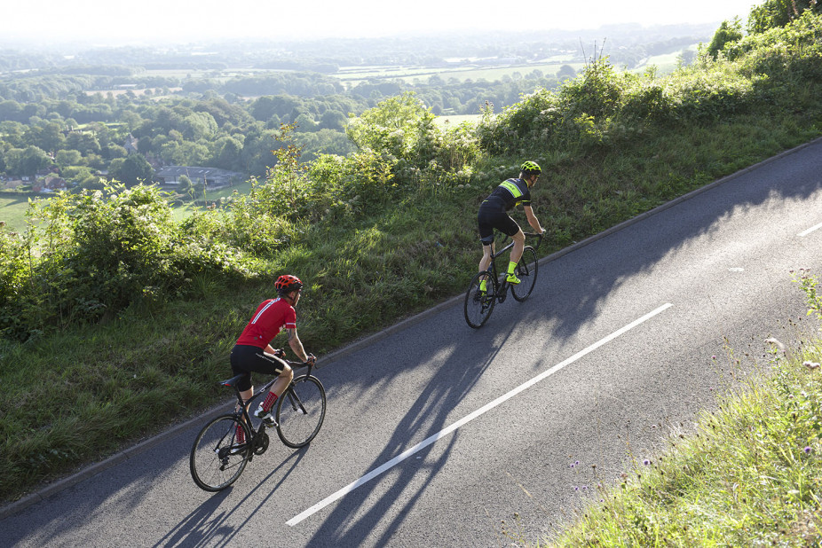 Two cyclists riding together on their Orro Bikes up a steep hill on a hot summers day