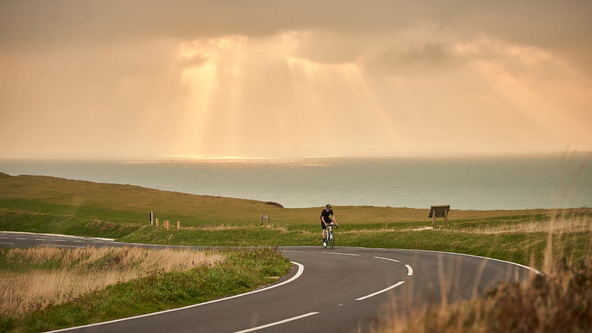 A cyclist riding a Orro Carbon Fibre Road Bike through a seaside coastal road whilst wearing a black Orro Cycling Jersey