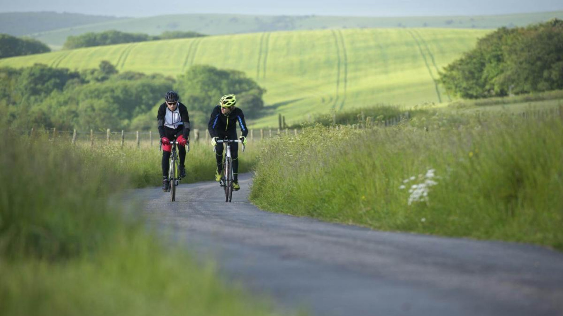 Two cyclists riding together on an empty country road on a clear summers day